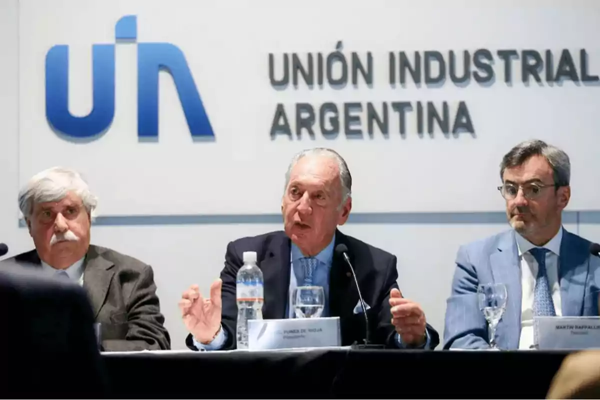 Tres hombres sentados en una mesa durante una conferencia de prensa en la Unión Industrial Argentina.