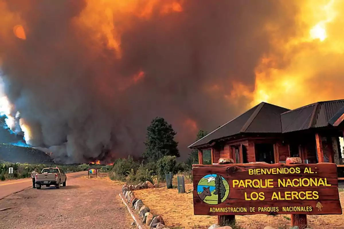 Un incendio forestal en el Parque Nacional Los Alerces con un cielo cubierto de humo y llamas mientras una camioneta está estacionada en el camino.