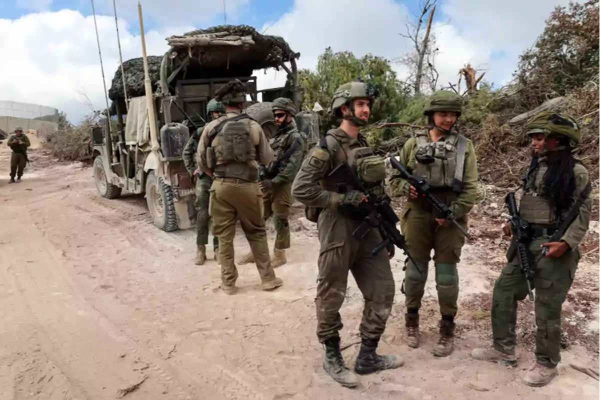 Un grupo de soldados con equipo militar se encuentra junto a un vehículo en un camino de tierra.