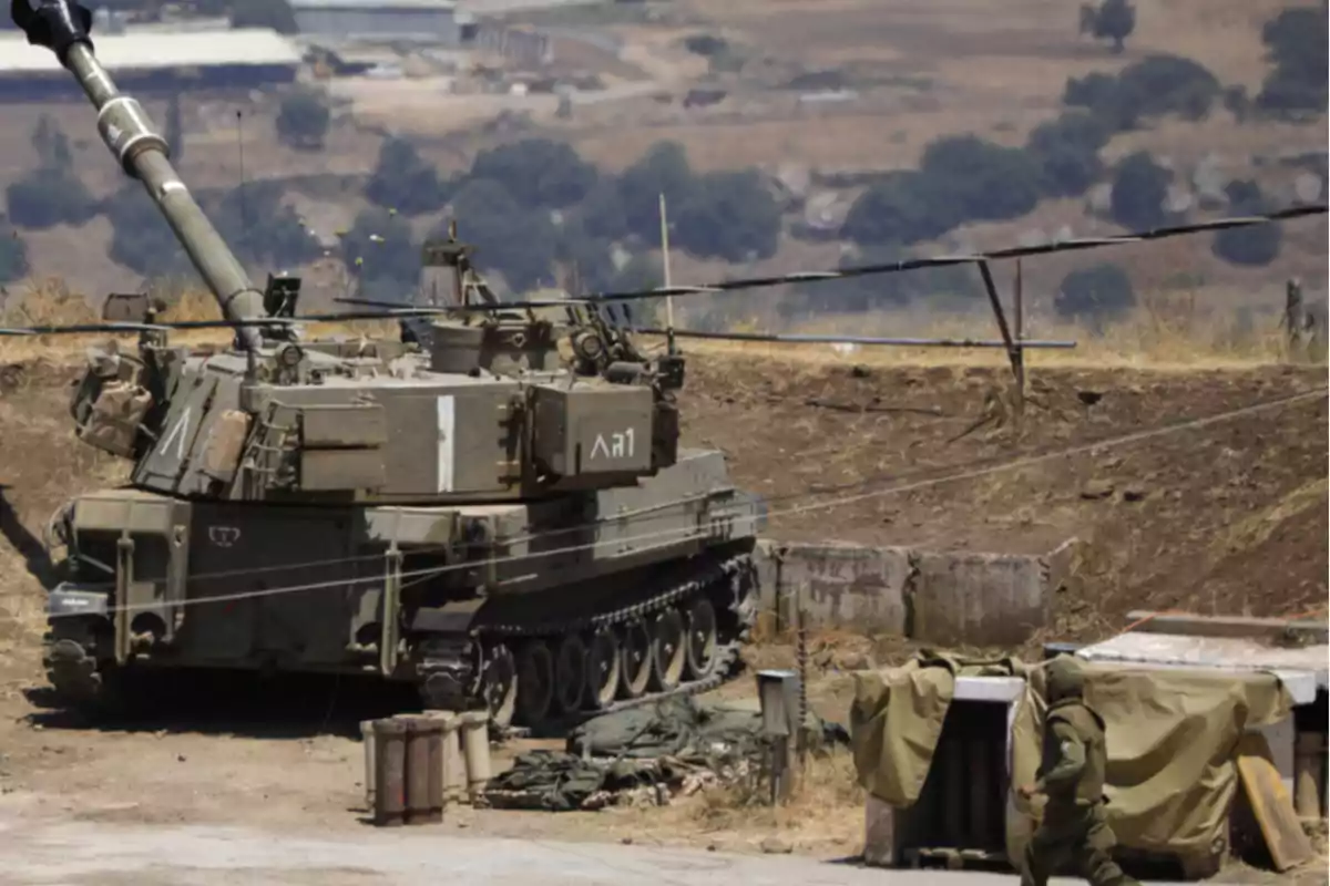 Un tanque militar en un terreno árido con un soldado caminando cerca.