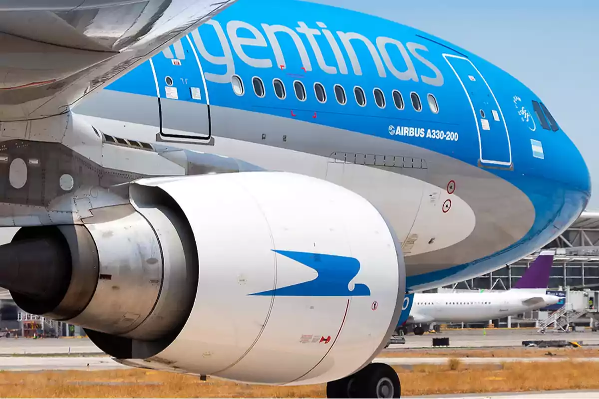 Un avión de pasajeros en un aeropuerto con el logo de una aerolínea en el fuselaje y el motor.