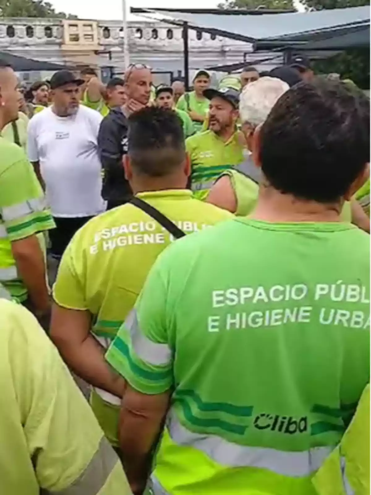 Un grupo de trabajadores de limpieza urbana con uniformes verdes se reúne al aire libre.