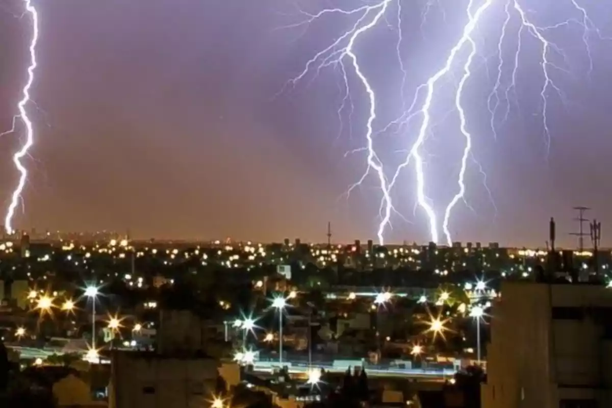 Tormenta eléctrica sobre una ciudad iluminada por la noche con varios rayos cayendo desde el cielo.