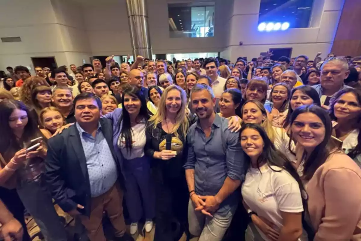 Un grupo numeroso de personas sonríe para una foto en un evento en un espacio interior iluminado.