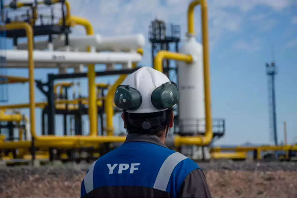 Trabajador de YPF con casco y protección auditiva frente a instalaciones industriales.