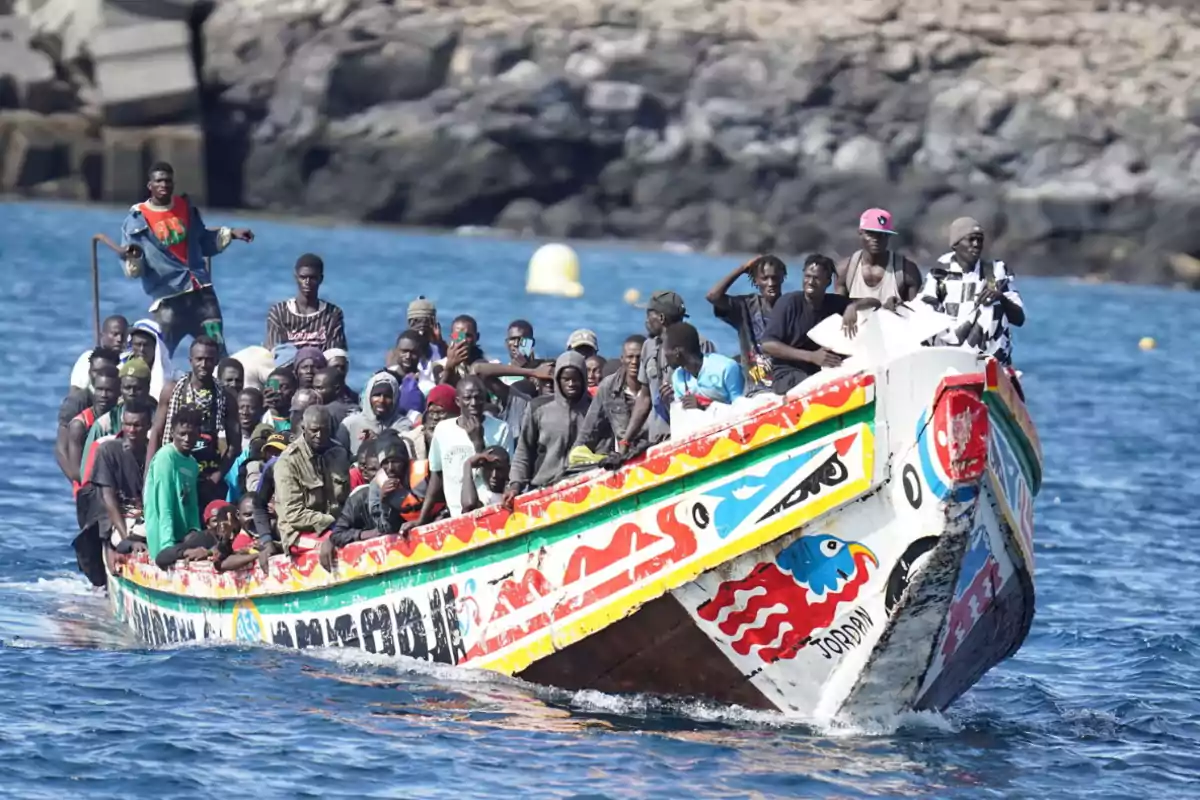 Un grupo de personas viaja en una colorida embarcación sobre el agua con un fondo rocoso.