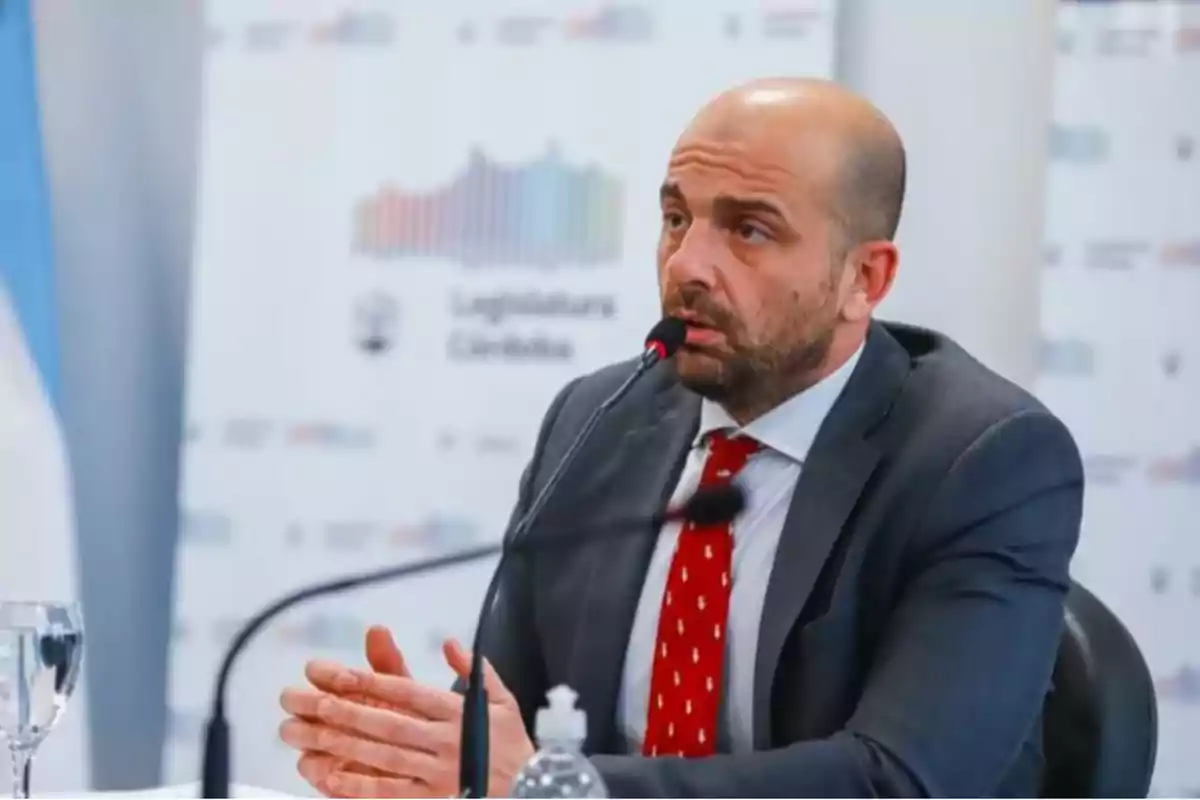 Un hombre calvo con barba y traje oscuro habla en un micrófono durante una conferencia de prensa.