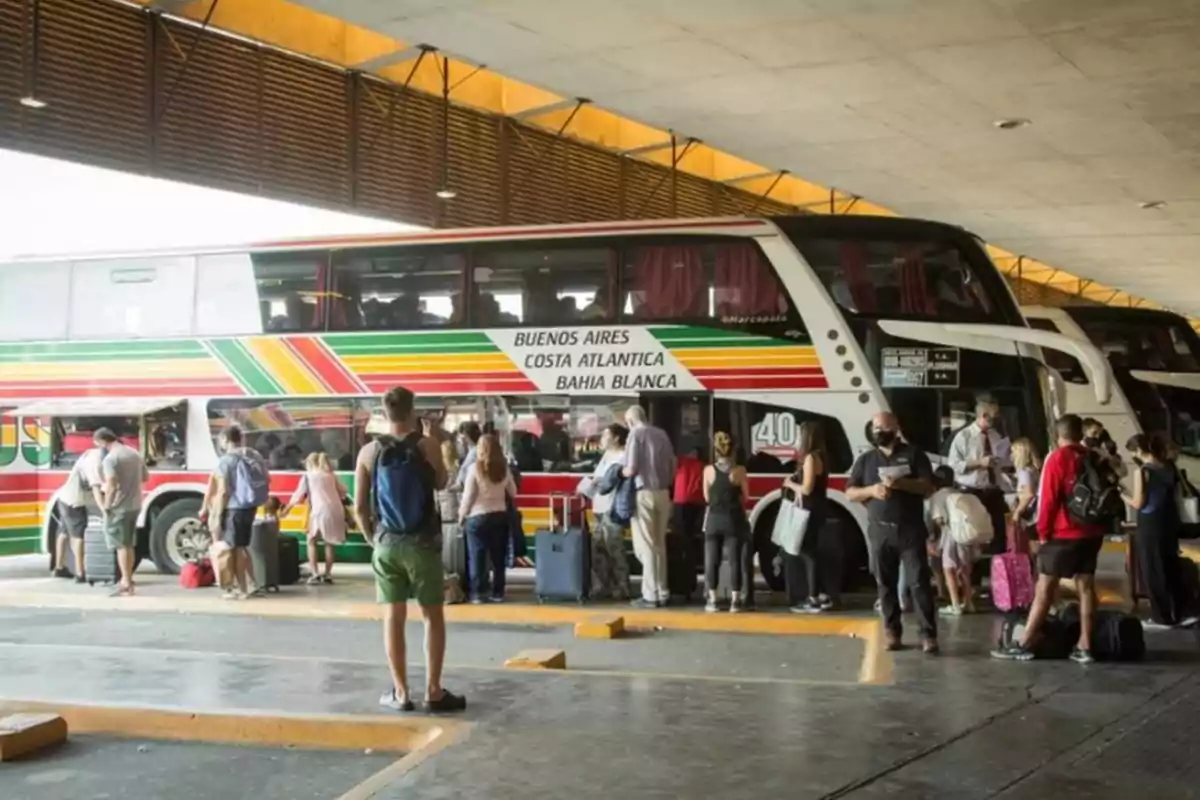 Personas haciendo fila para abordar un autobús de dos pisos en una terminal de transporte.