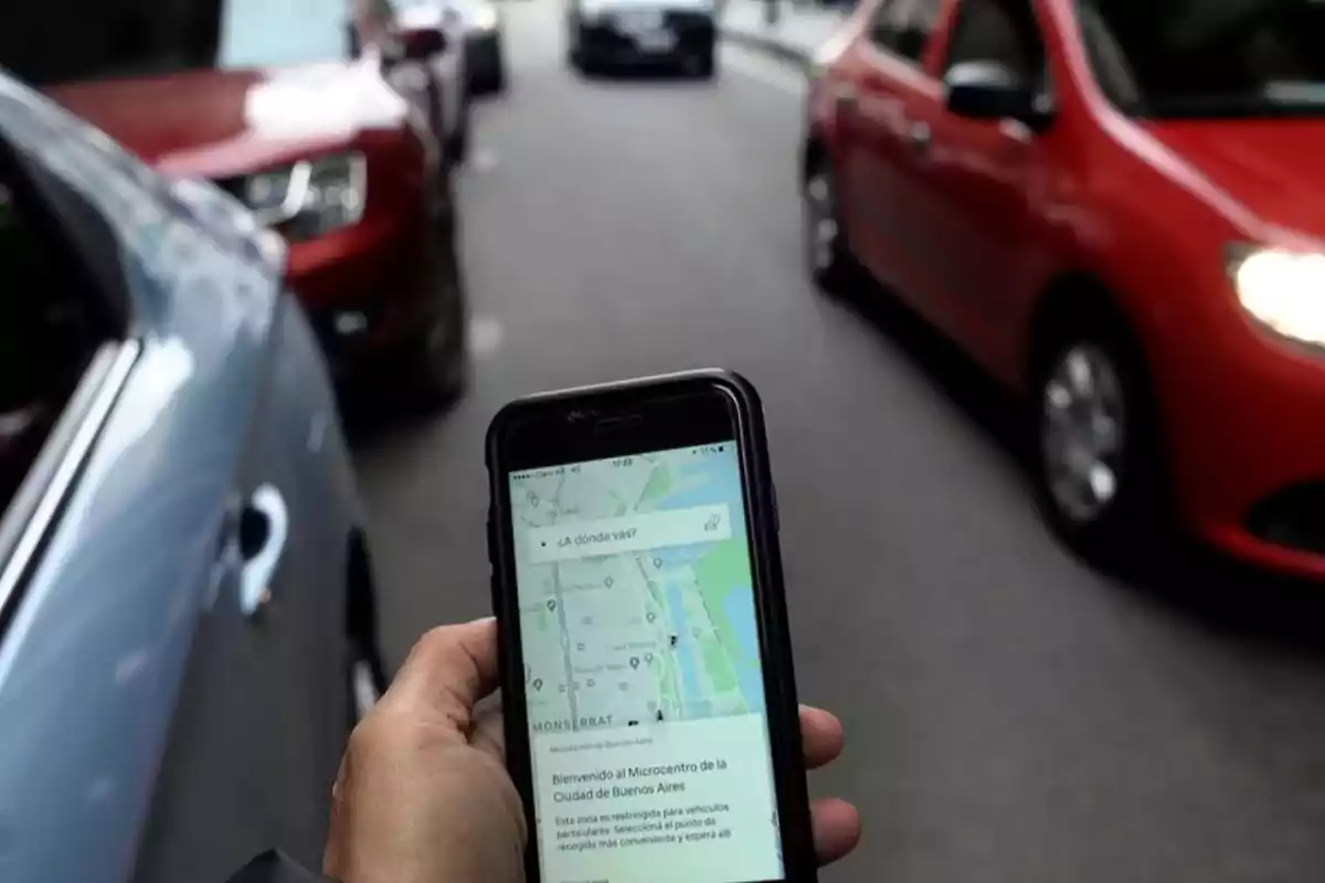 Persona sosteniendo un teléfono con una aplicación de mapas abierta mientras está rodeada de autos en una calle.