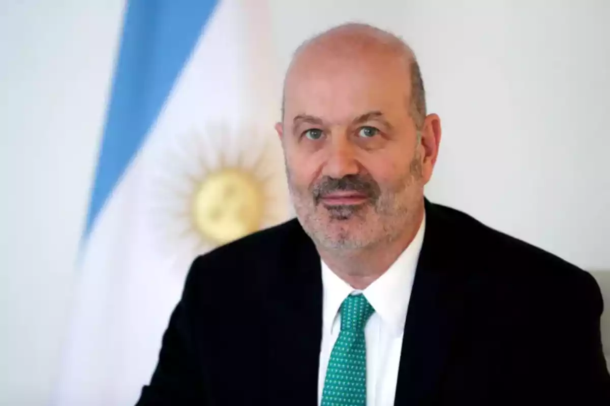 Hombre de traje oscuro y corbata verde frente a una bandera de Argentina.