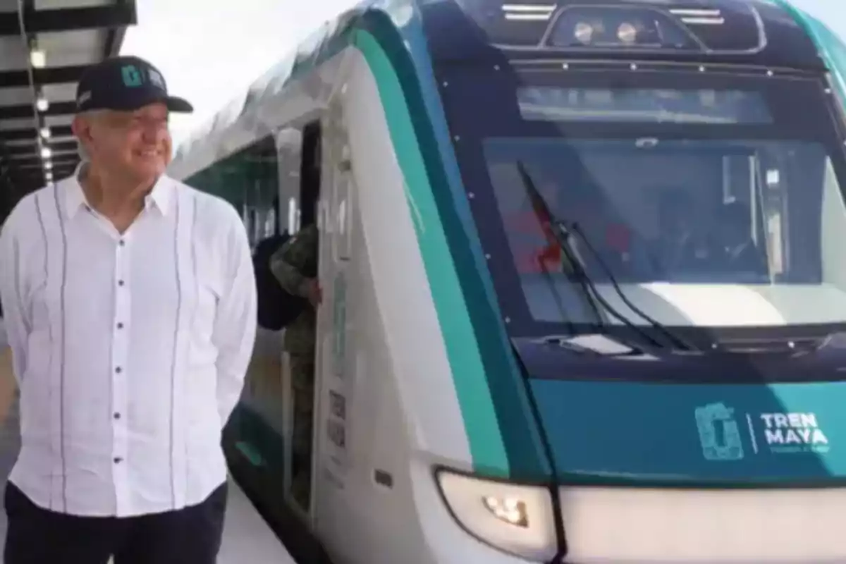 Un hombre con camisa blanca y gorra negra está de pie junto a un tren moderno en una estación.