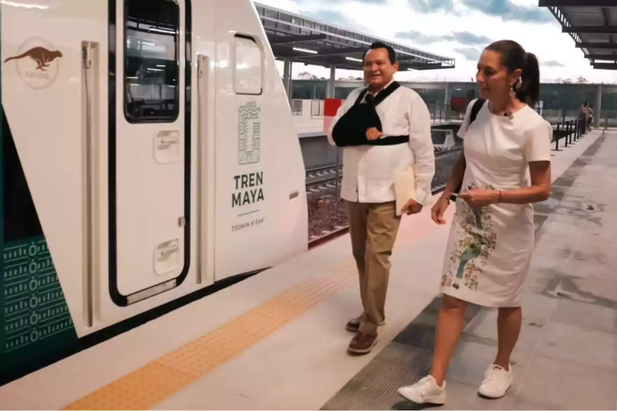 Dos personas caminando junto a un tren del Tren Maya en una estación moderna.