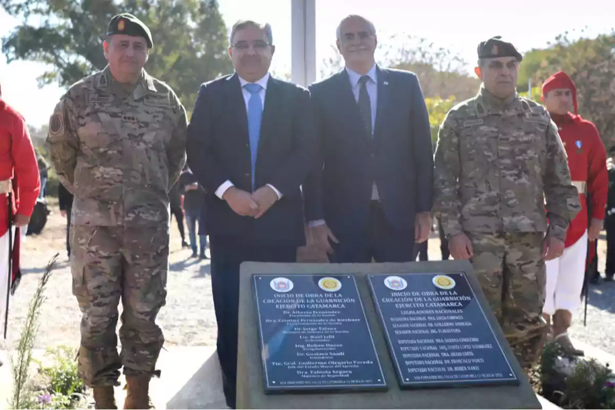 Un grupo de personas, algunas en uniforme militar, posan junto a una placa conmemorativa al aire libre.