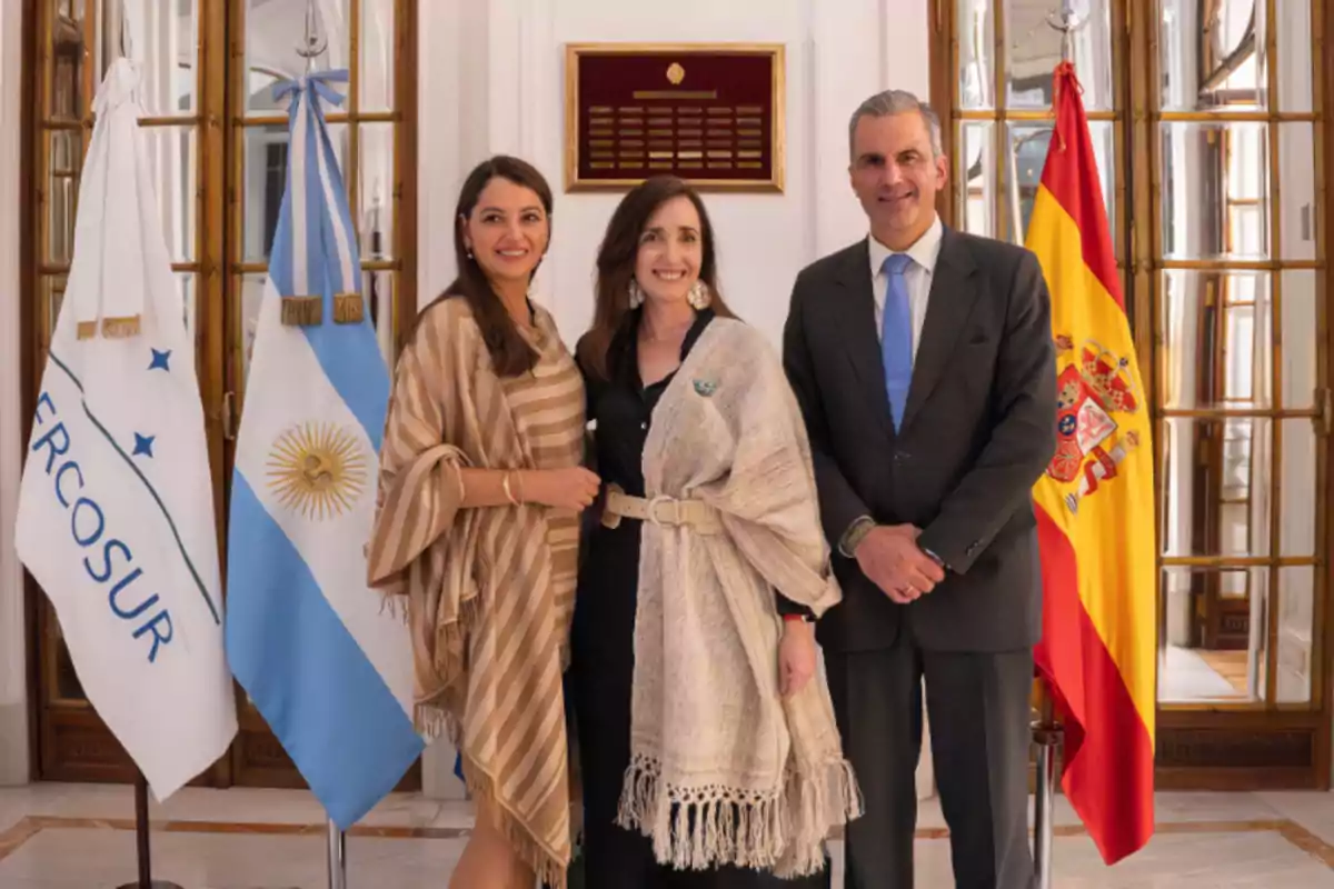 Tres personas posan frente a las banderas de Mercosur, Argentina y España en un entorno formal.