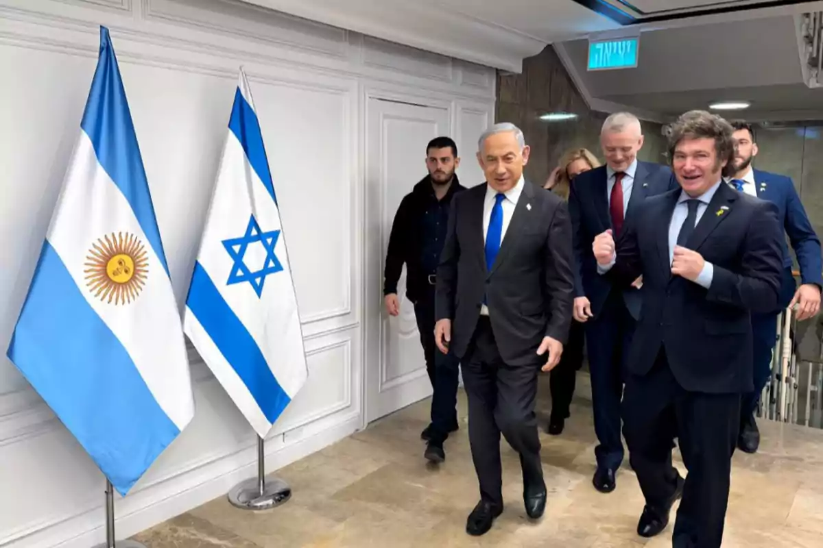 Un grupo de personas caminando junto a las banderas de Argentina e Israel en un edificio.