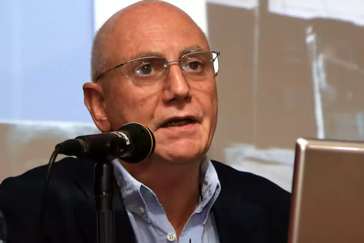 Hombre calvo con gafas hablando en un micrófono durante una presentación.