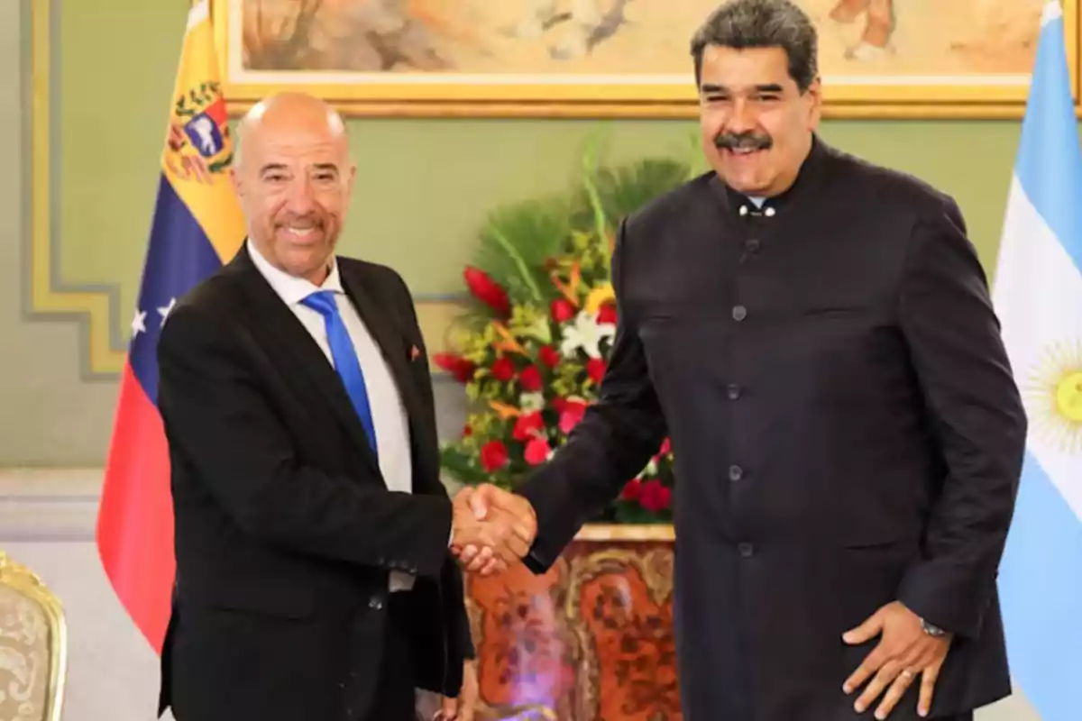 Dos hombres estrechándose la mano en un entorno formal con banderas de Venezuela y Argentina de fondo.