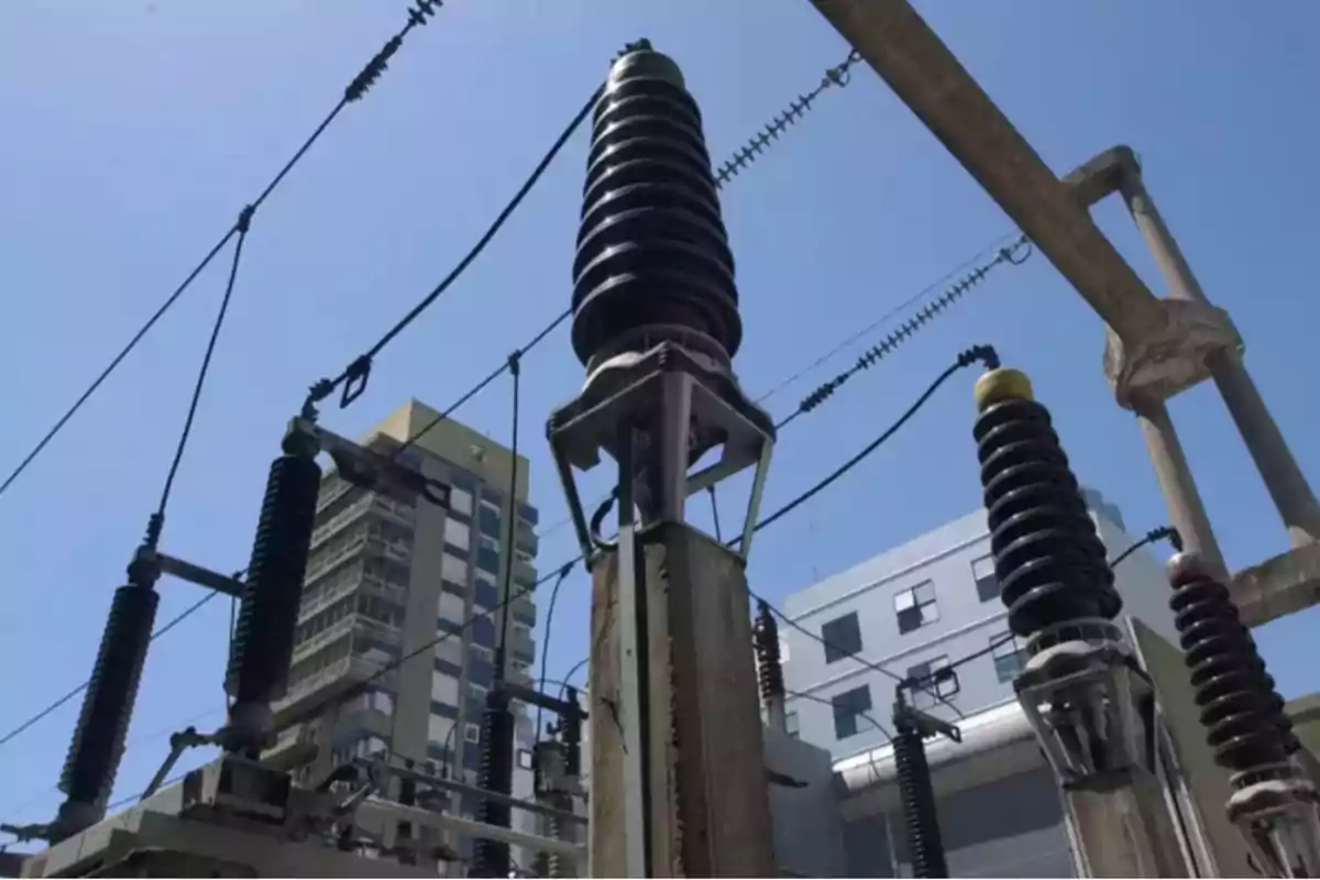 Vista de una subestación eléctrica con aisladores y cables de alta tensión en un entorno urbano.