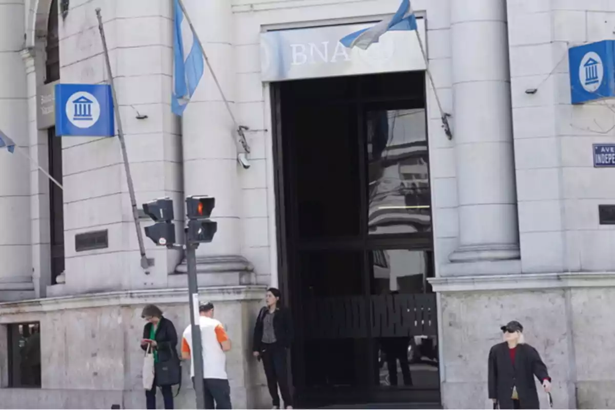 Fachada de un banco con personas caminando y un semáforo en la esquina.