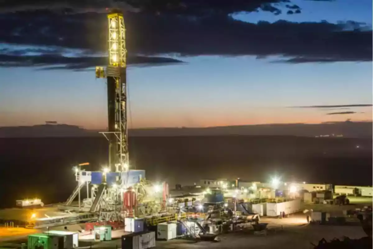 Plataforma de perforación iluminada al anochecer en un campo petrolero.