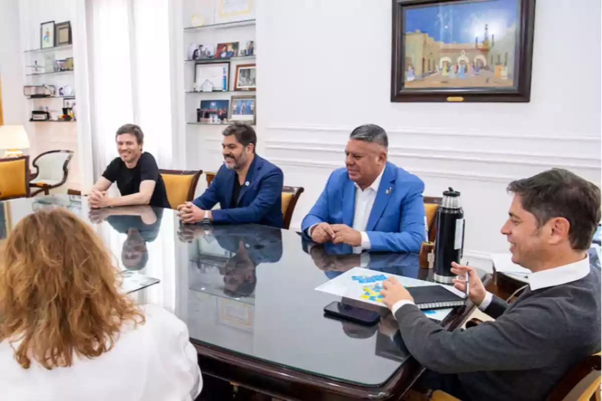 Un grupo de personas sentadas alrededor de una mesa en una reunión en una oficina decorada con cuadros y estanterías.