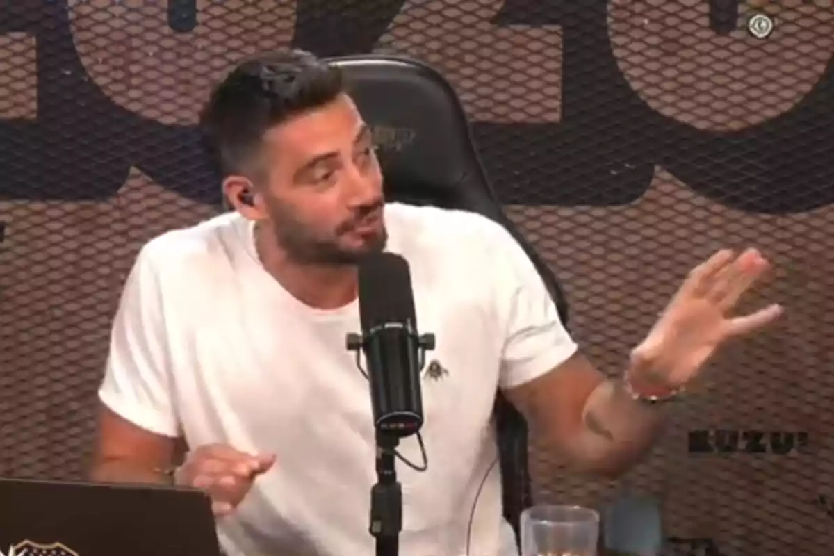 Un hombre con camiseta blanca hablando frente a un micrófono en un estudio.