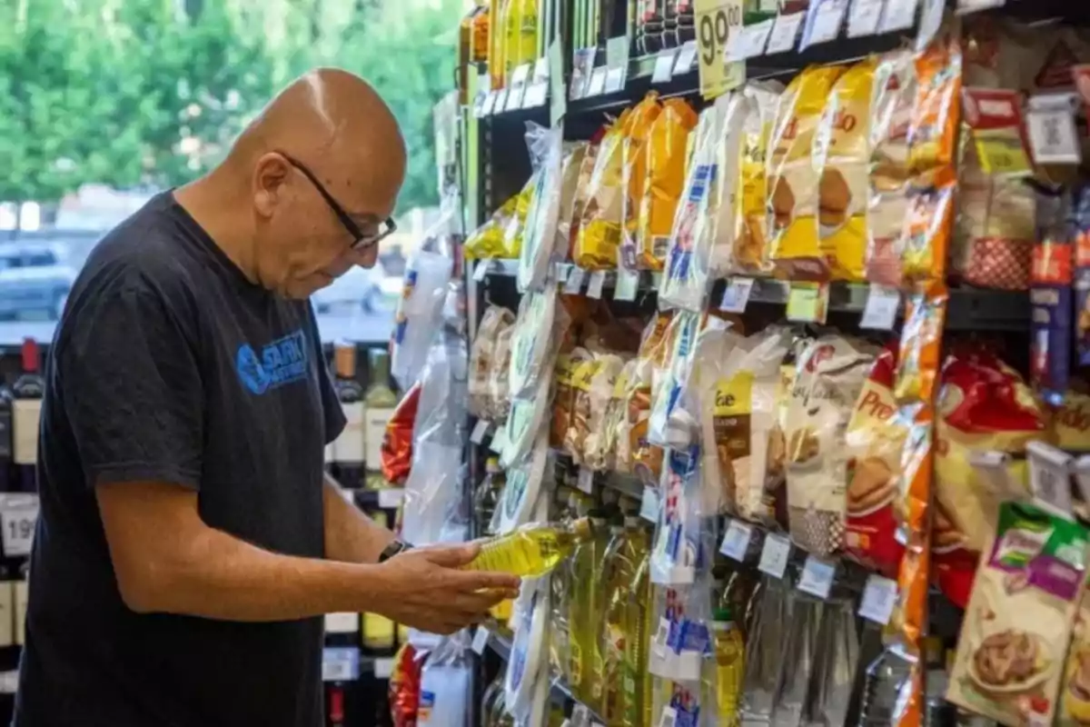 Un hombre revisa una botella de aceite en el pasillo de un supermercado lleno de productos.