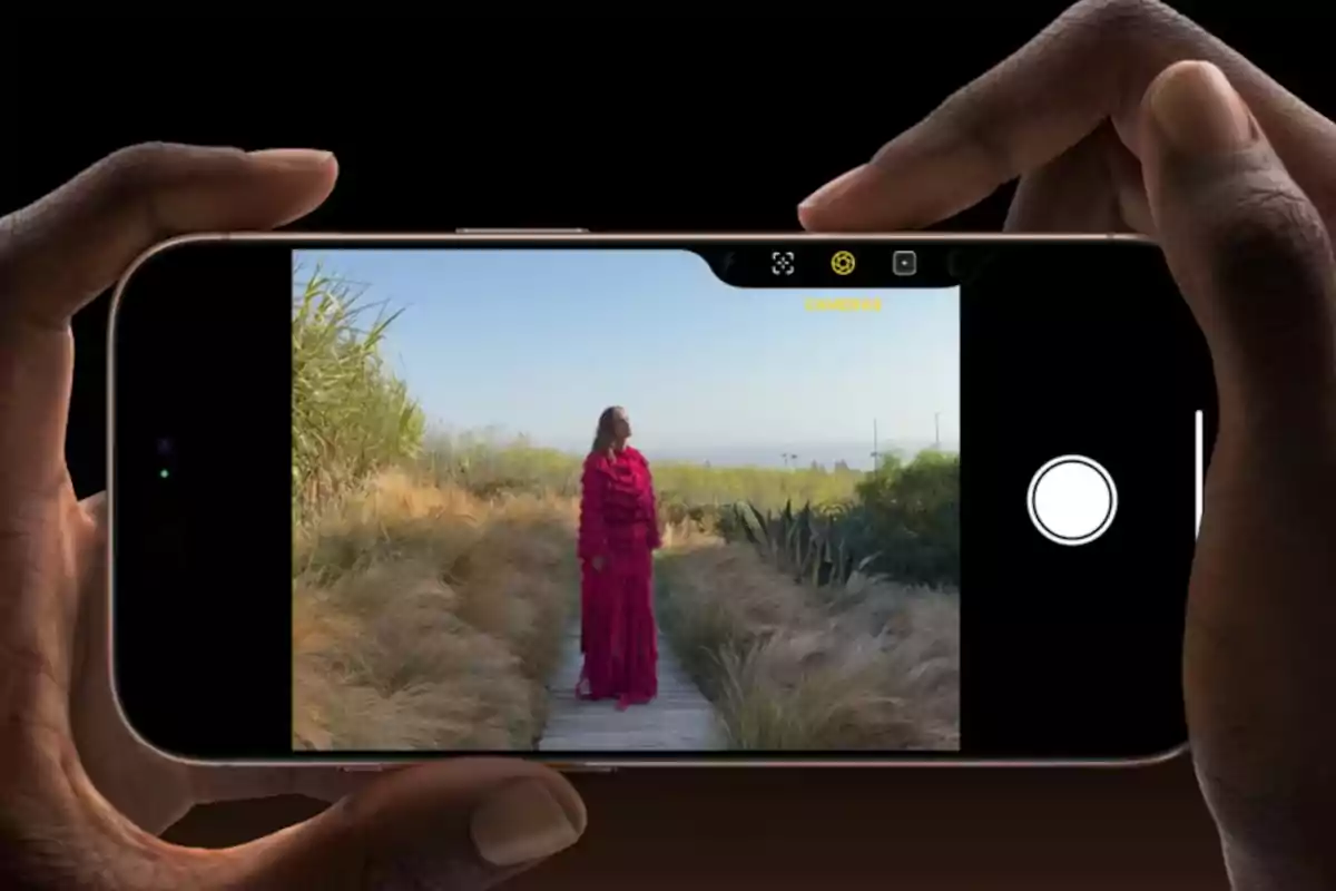 Una persona con un vestido rojo posando en un camino rodeado de vegetación mientras es fotografiada con un teléfono móvil.