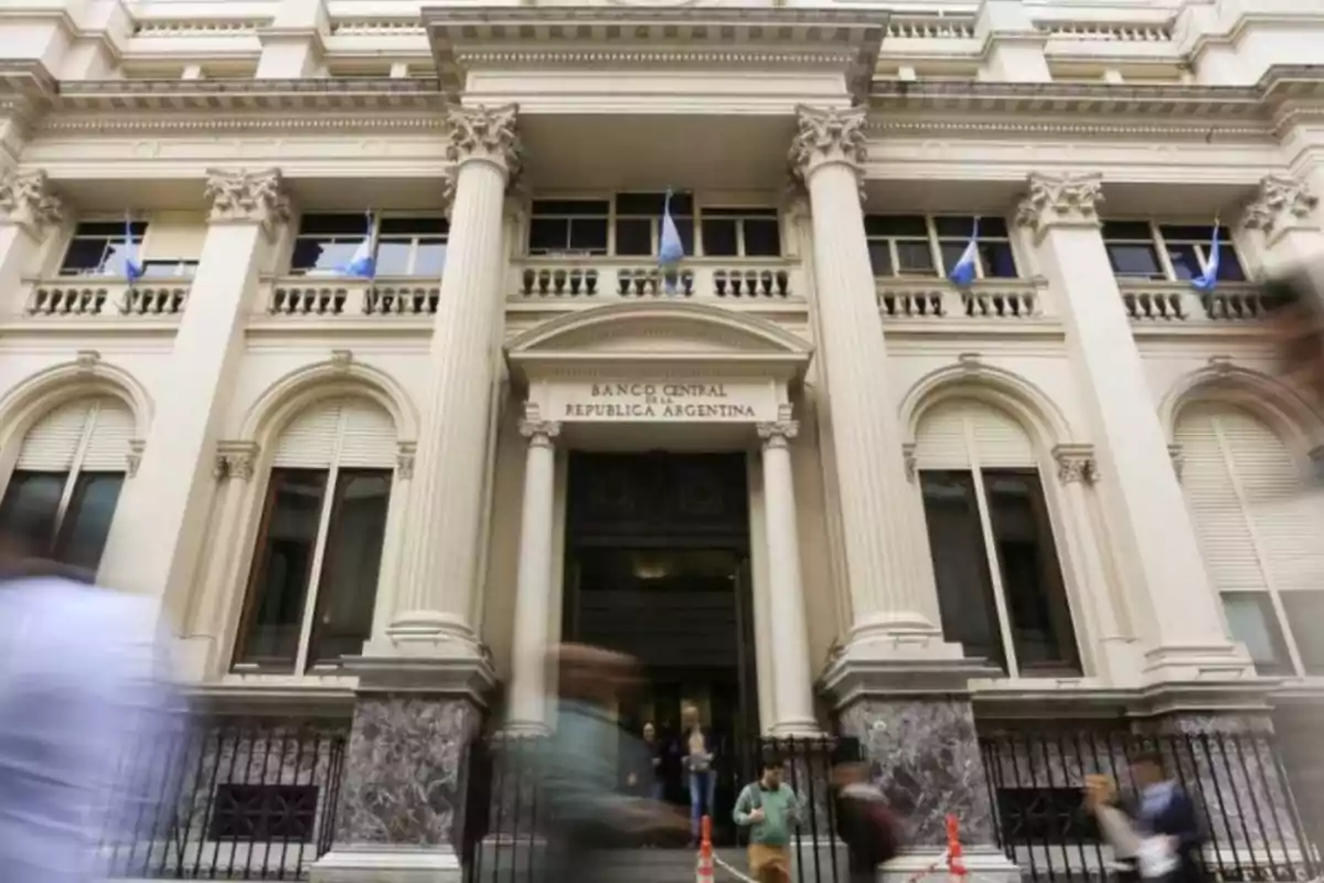 Fachada de un edificio con columnas clásicas y personas caminando al frente.