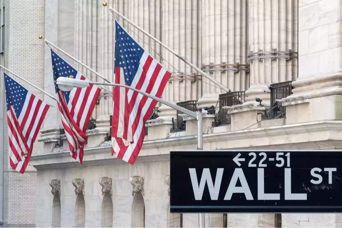 Banderas de Estados Unidos ondean frente a un edificio con columnas y un letrero de Wall Street.