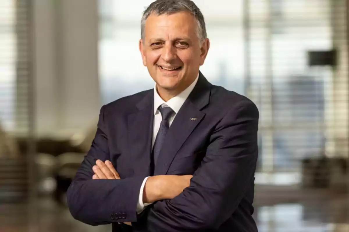 Hombre de traje sonriendo con los brazos cruzados en una oficina.