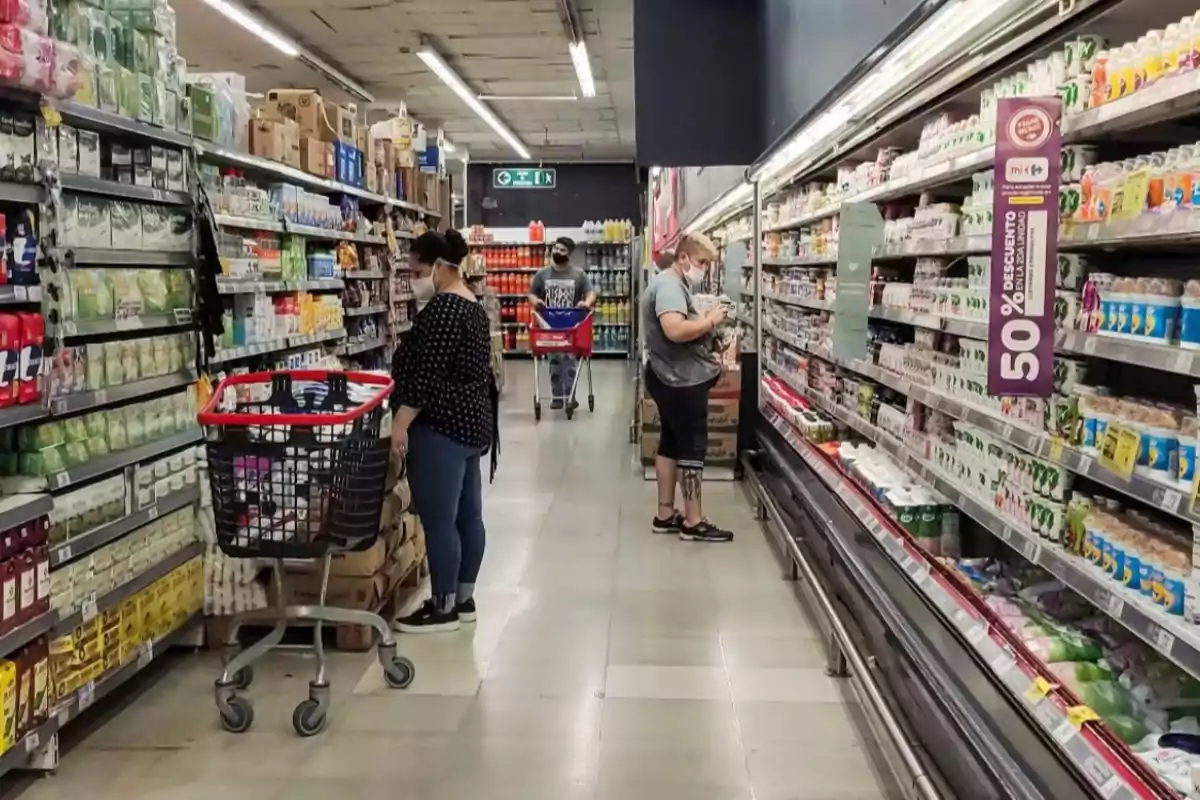 Personas comprando en un supermercado, algunas con mascarillas, mientras revisan productos en los estantes.