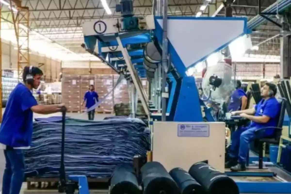 Trabajadores en una fábrica operando maquinaria industrial y moviendo materiales.