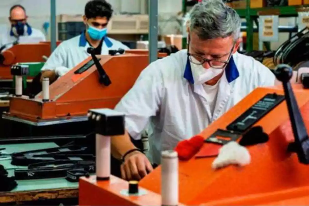 Trabajadores en una fábrica usando mascarillas y operando maquinaria industrial.