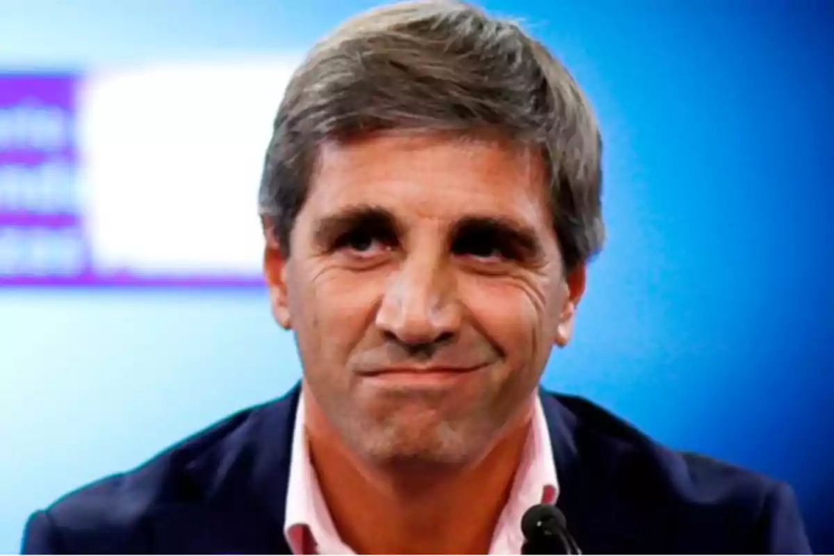 Un hombre de cabello canoso y expresión seria frente a un fondo azul.