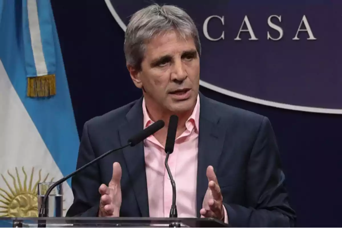 Un hombre de cabello canoso y traje oscuro habla en un podio con micrófonos frente a una bandera argentina.