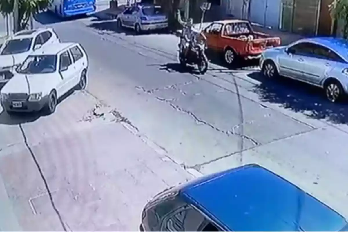 Una calle con varios vehículos estacionados y una motocicleta en movimiento.