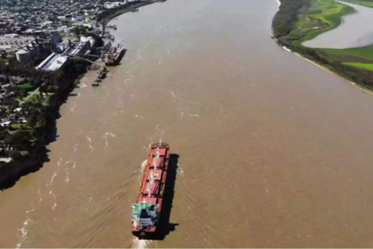 Vista aérea de un río con un barco navegando cerca de la orilla, donde se observan instalaciones industriales y áreas verdes.