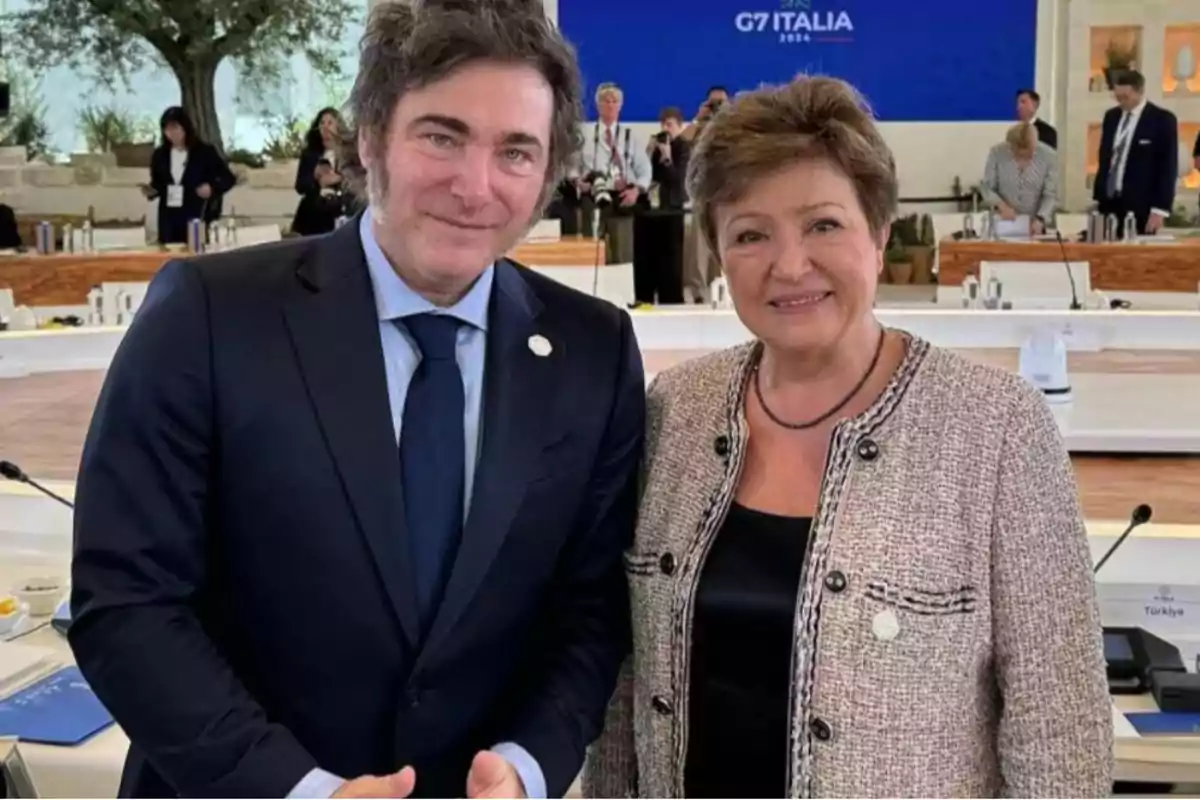 Dos personas posan juntas en un evento del G7 en Italia 2024, con un fondo de asistentes y una pantalla azul.