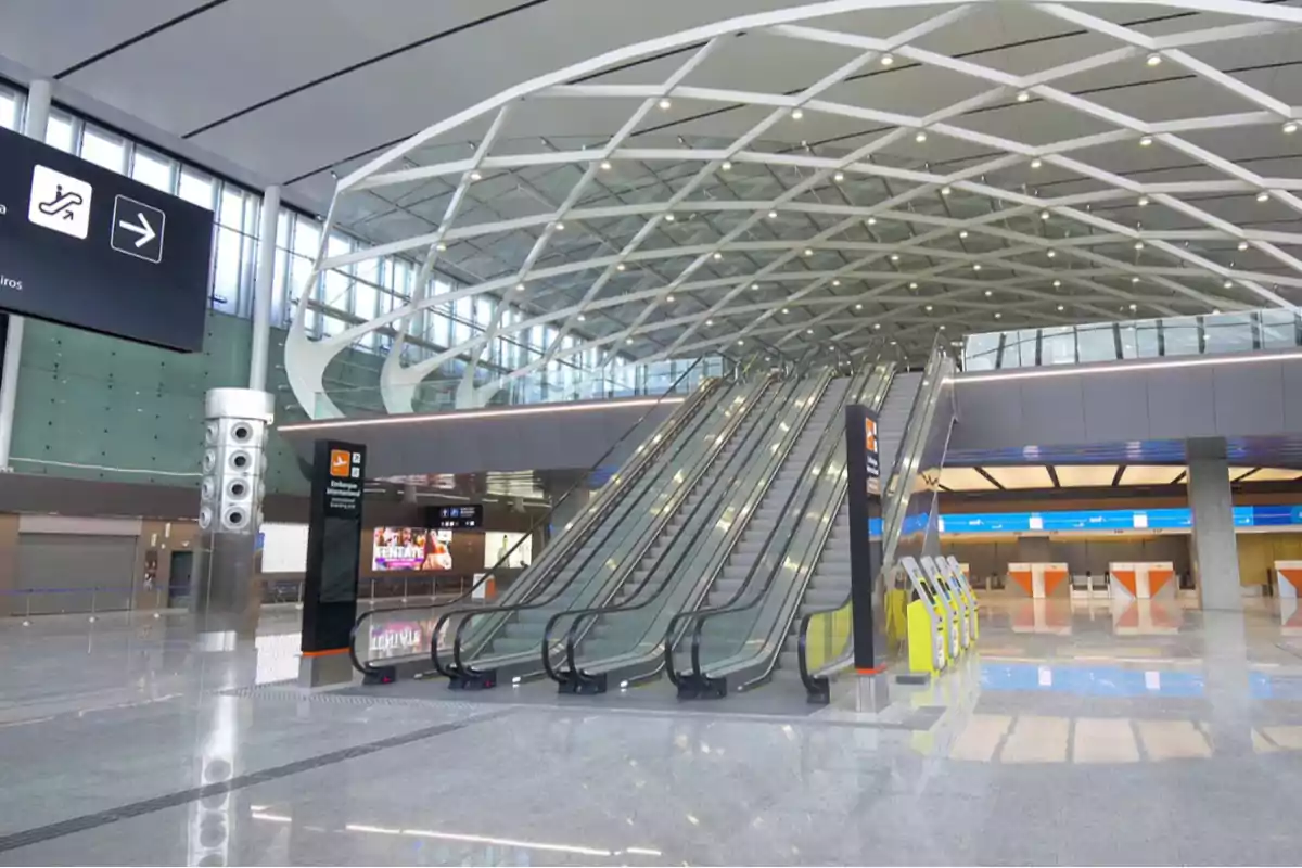 Un moderno vestíbulo de aeropuerto con escaleras mecánicas y techo de diseño geométrico.