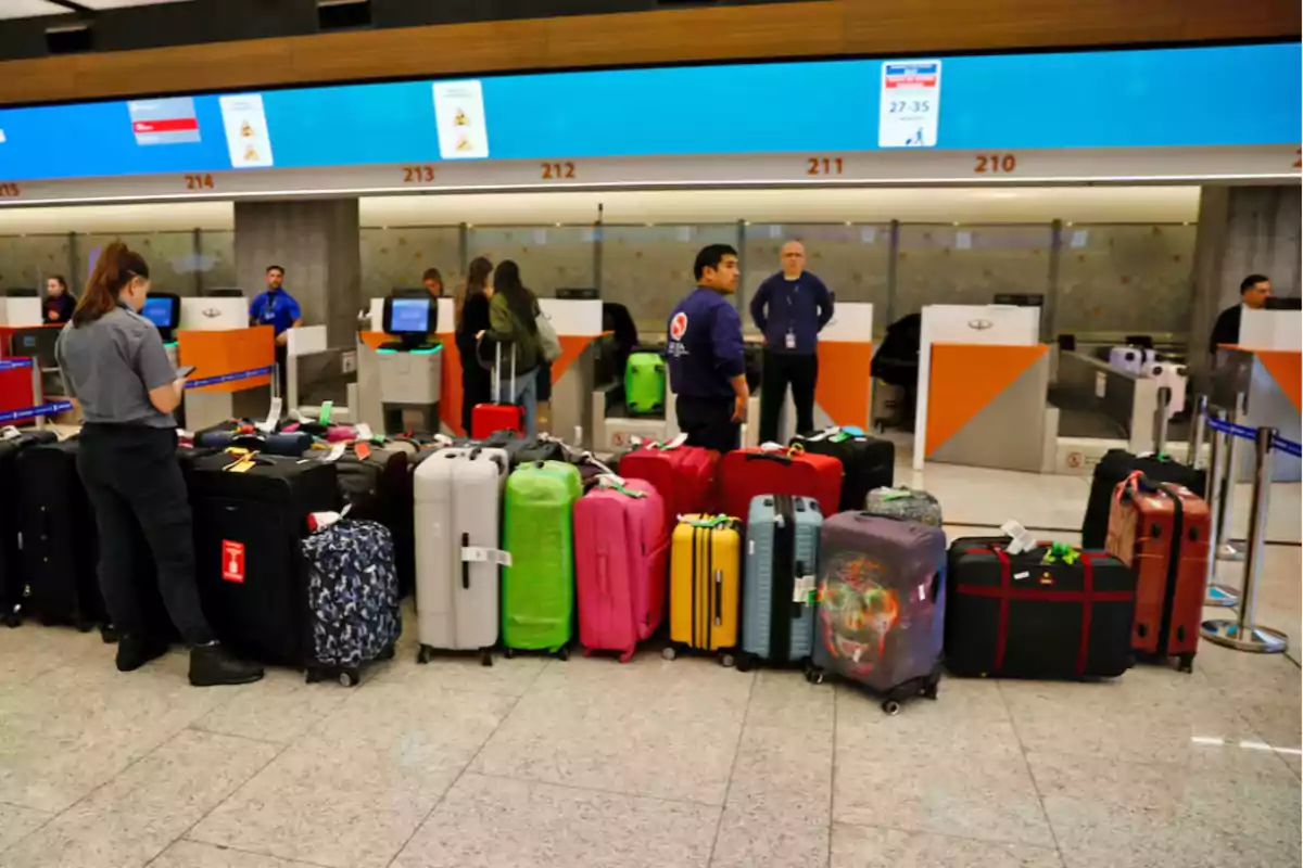 Personas en un mostrador de facturación de equipaje en un aeropuerto con varias maletas alineadas en el suelo.