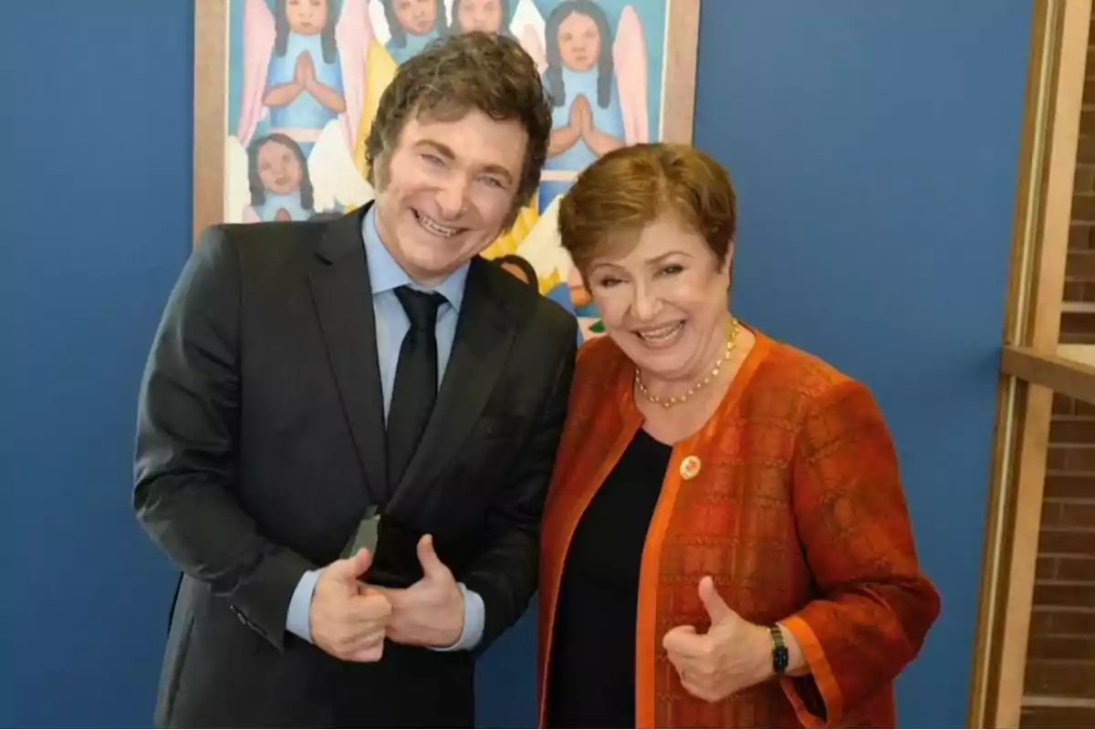 Dos personas sonrientes posan juntas frente a una pintura colorida, ambas haciendo el gesto de pulgares arriba.