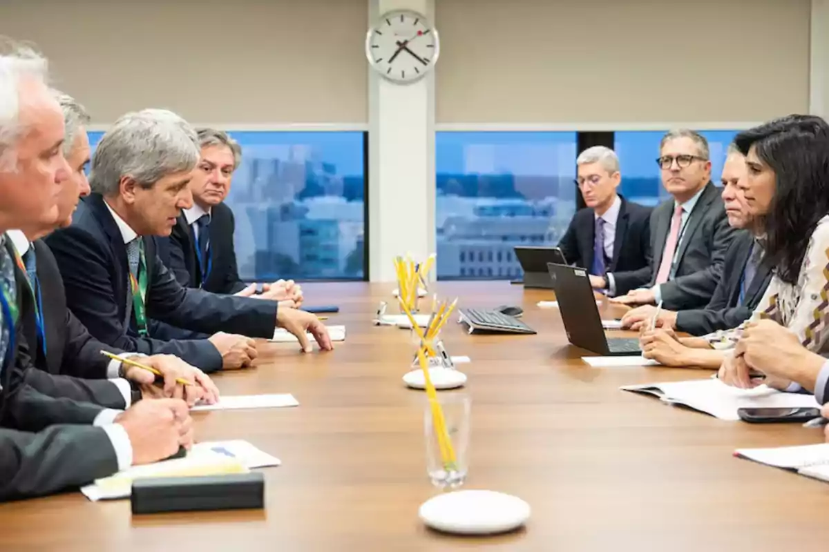 Un grupo de personas en una reunión de negocios sentadas alrededor de una mesa de conferencias con papeles y computadoras portátiles.