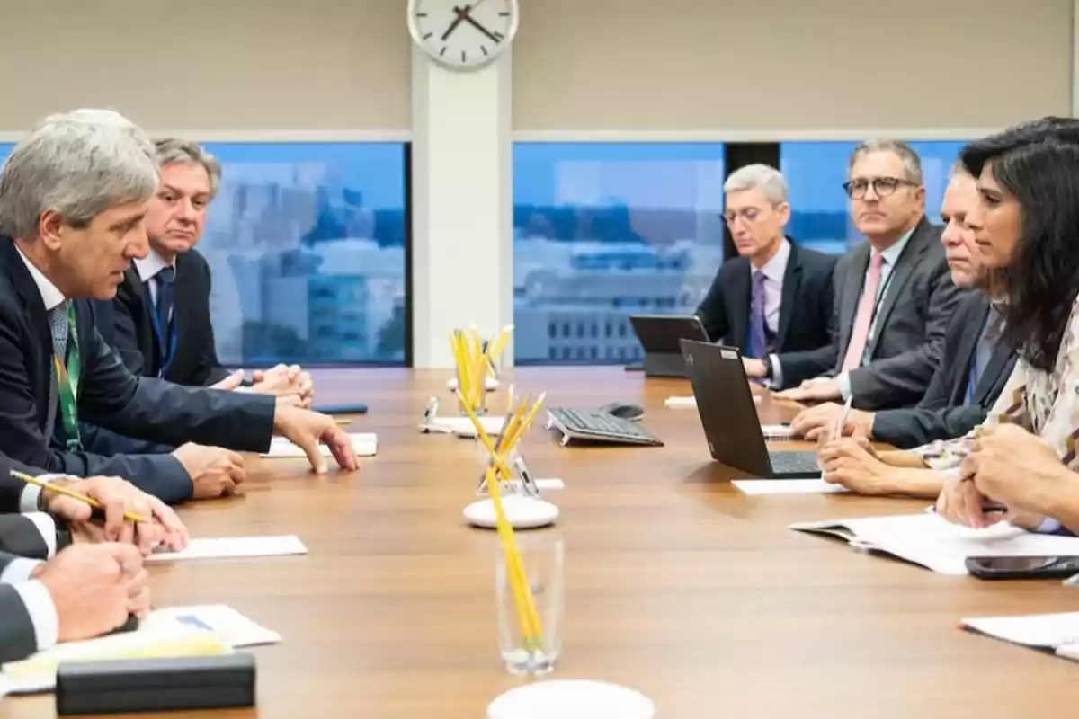 Un grupo de personas en una reunión de trabajo sentadas alrededor de una mesa con papeles y computadoras portátiles.