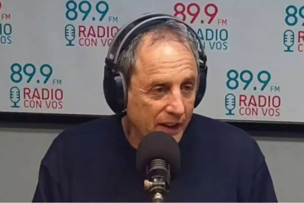 Hombre con auriculares hablando frente a un micrófono en un estudio de radio con el logo de 