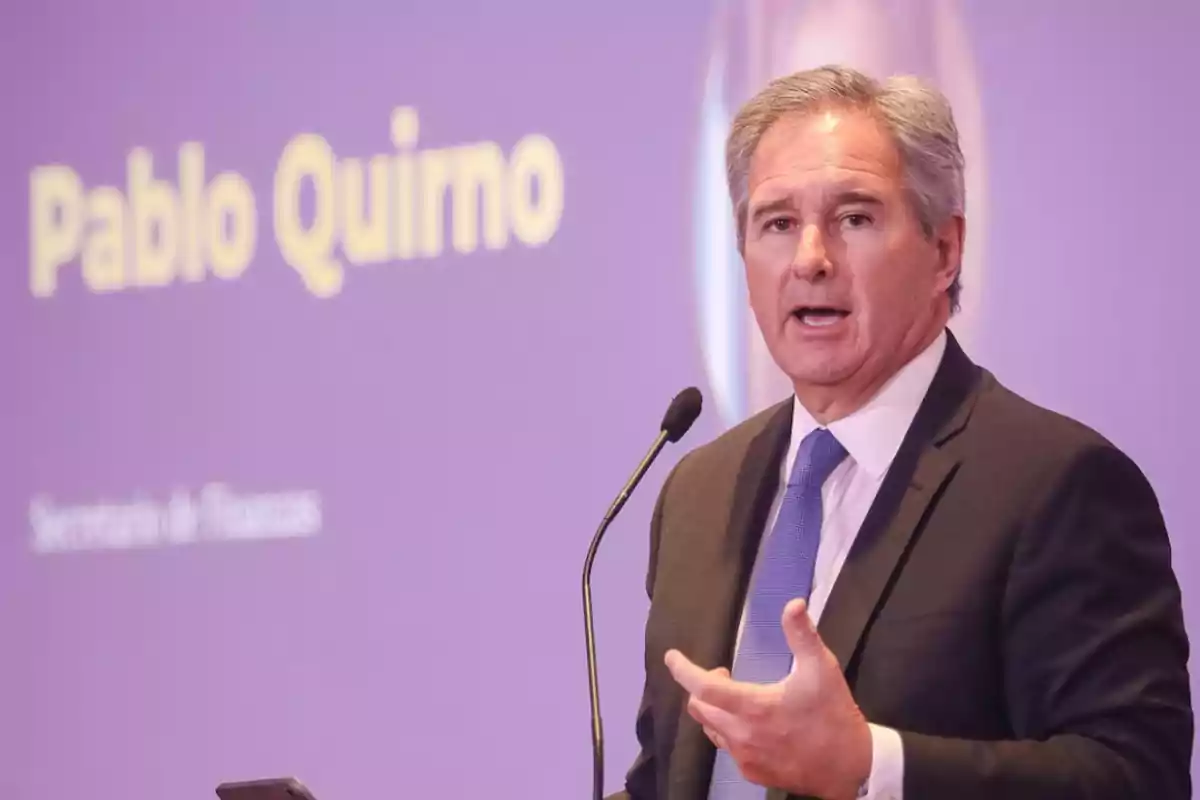 Un hombre en traje hablando en un podio con un fondo morado.