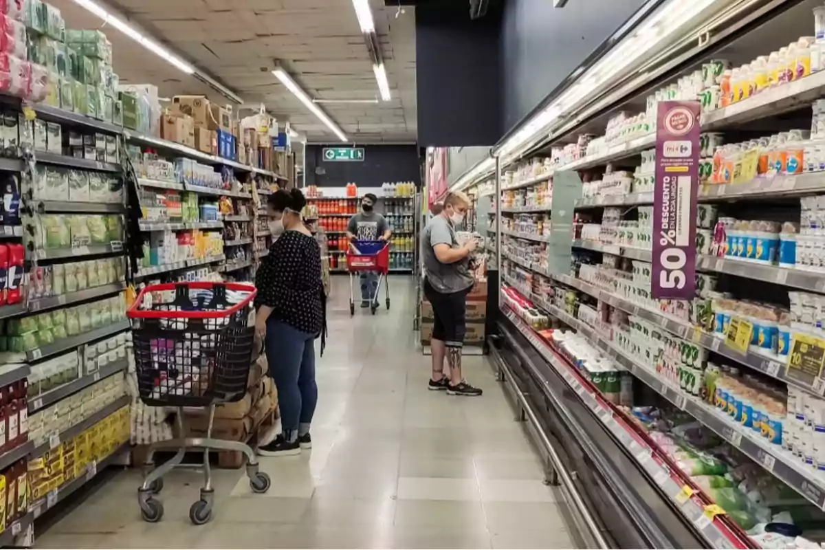 Personas comprando en un pasillo de supermercado con estantes llenos de productos y carritos de compras.