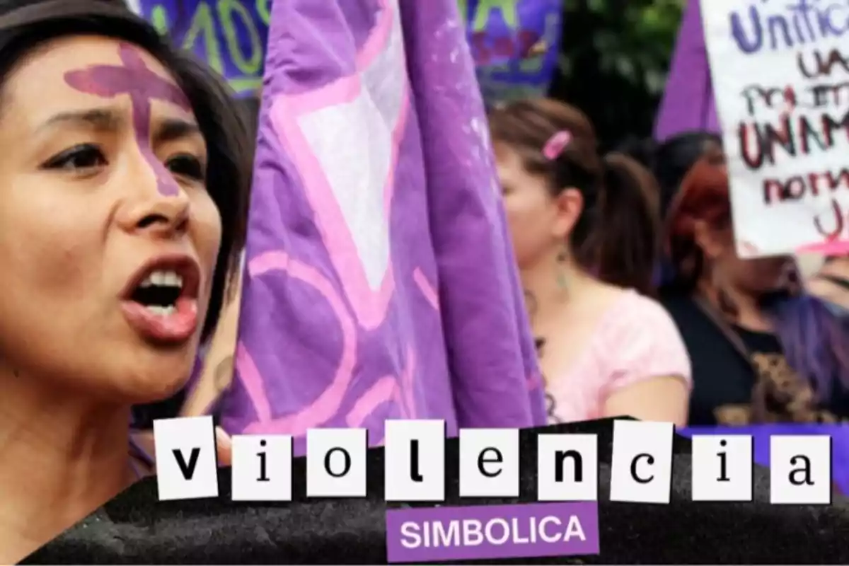 Una mujer con una cruz morada pintada en la frente sostiene una bandera morada en una manifestación, con el texto "violencia simbólica" en la parte inferior.