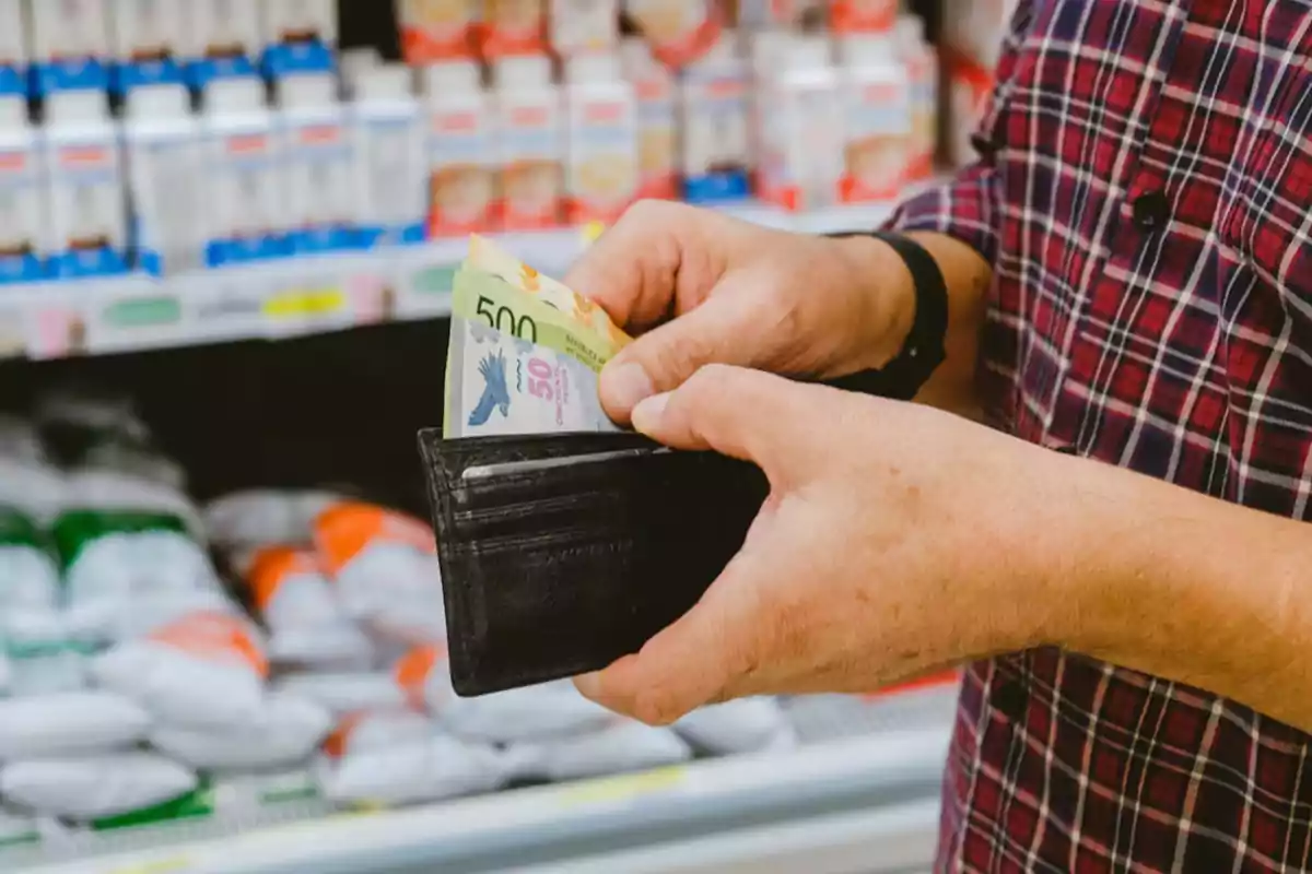 Persona sacando billetes de una billetera en un supermercado.