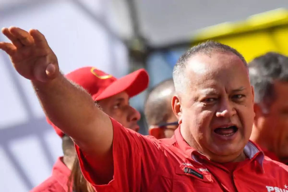 Un hombre con camisa roja gesticulando con el brazo extendido, rodeado de otras personas con gorras rojas.